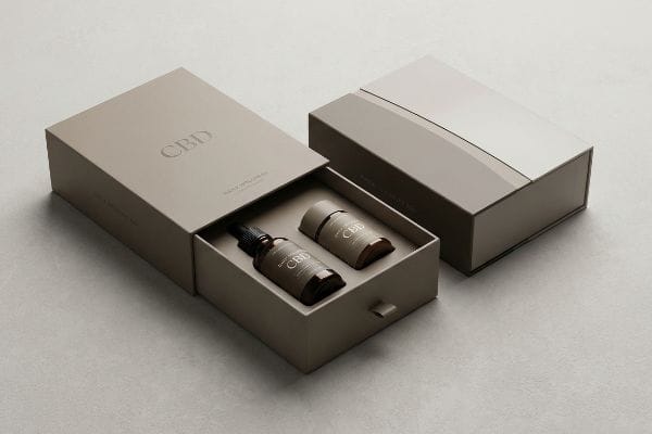 CBD Drawer Packaging Matte taupe drawer-style CBD packaging, embossed 'Cbd Daily Wellbeing', with dropper bottle and capsule.