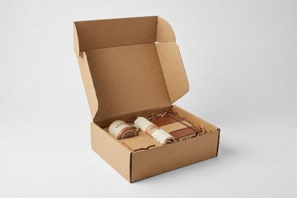 Premium-Unboxing-Set Ein geöffneter brauner Kraftpapier-Versandkarton zeigt eine Keramiktasse mit der Aufschrift „Chill“, ein zusammengerolltes Handtuch und ein Notizbuch aus Leder, eingebettet in zerkleinertes Füllmaterial für Abonnement-Sets.