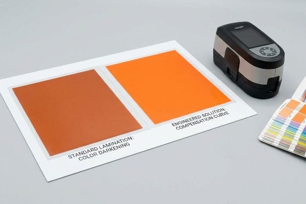Ein Spektralphotometer misst laminierte orangefarbene Farbmuster und vergleicht „Standardlaminierung: Farbverdunkelung“ mit „Technische Lösung: Kompensationskurve“.