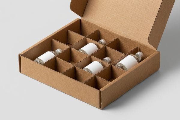 An open brown corrugated box with divider inserts holding small clear glass bottles with white labels, showcasing product organization and protection.