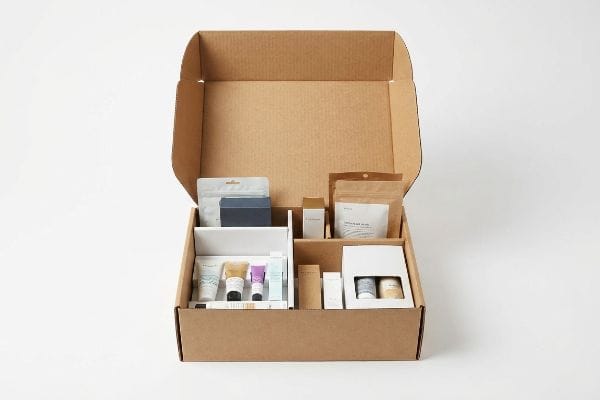 開口部のある段ボール製のディスプレイボックスには、白い仕切りと特注の型抜きインサートによって整理された様々な美容製品が陳列されている。.