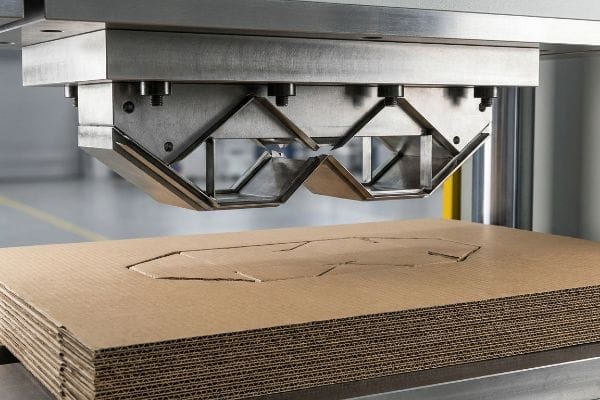Corrugated Die-Cutting Process A steel die-cutting blade precisely stamps out shapes from a stack of corrugated cardboard sheets, demonstrating the cut-die process for custom displays.