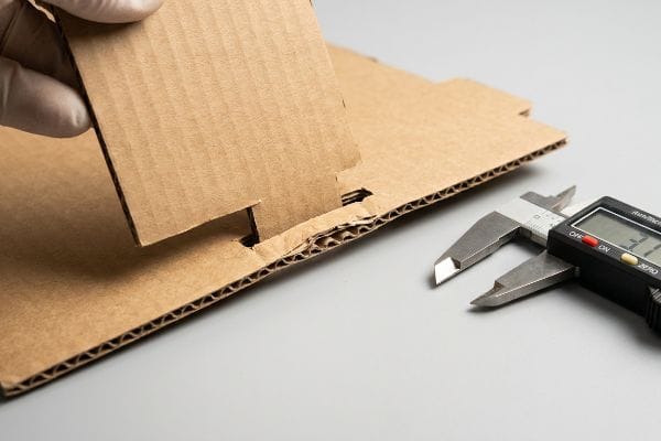 Cardboard Flute Thickness Measurement Corrugated cardboard interlocking pieces being measured by a digital caliper for flute thickness compensation.