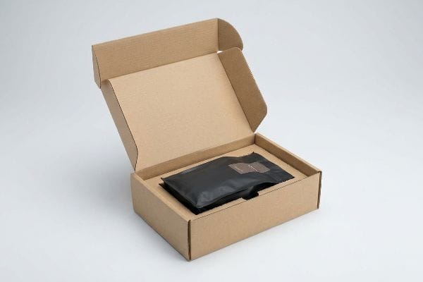 Coffee Bag Mailer Box Brown corrugated mailer box open with a black flexible pouch inside, ready for shipping coffee bags.