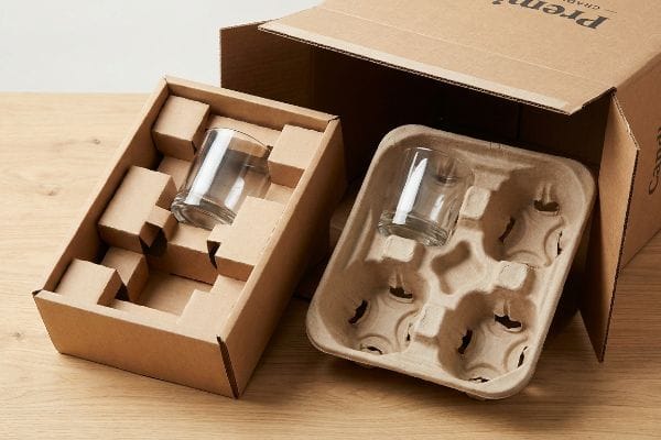 Candle Packaging Inserts Protection Two types of candle packaging inserts, corrugated cardboard and molded pulp, protect glass jars within an open shipping box.