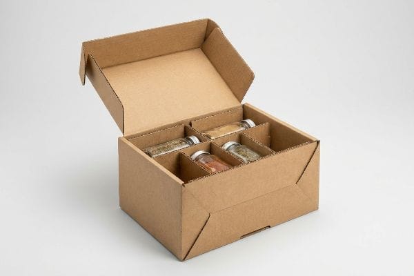 Brown corrugated cardboard box with internal dividers securely holding four glass spice jars, showcasing protective packaging.