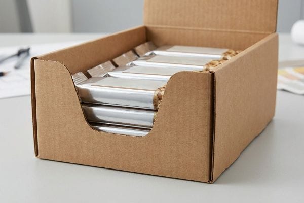 Product First Display Tray Brown corrugated cardboard display tray with a custom die-cut swoop front, showcasing silver-wrapped energy bars for impulse buys.