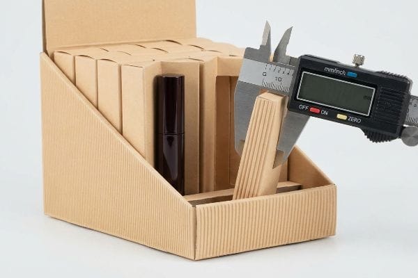 A digital caliper precisely measures the ribbed corrugated cardboard panel of a cosmetic box, highlighting the critical bulge for micro-clearance engineering.