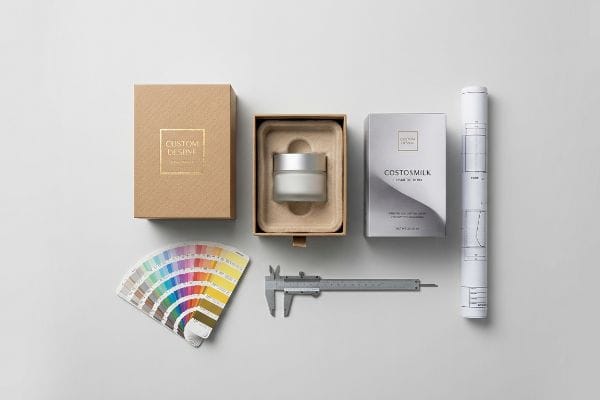 Cosmetic Packaging Design Tools Cosmetic packaging design layout with Custom Desire gold foil boxes, Costosmilk cream jar, color swatches, caliper, and blueprint.