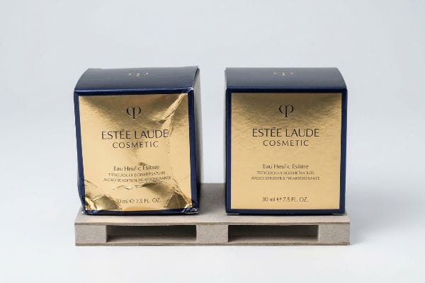 Dark blue Estée Laude Cosmetic Eau Heulic Esitare boxes, one with crumpled gold foil, 30 ml, on a cardboard pallet.