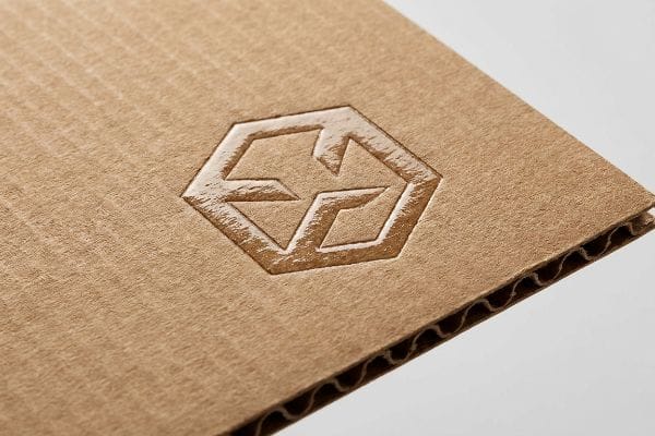 Debossed Corrugated Packaging Detail Brown corrugated cardboard features a deep, inward 3D debossed hexagonal logo, highlighting a premium tactile packaging design.