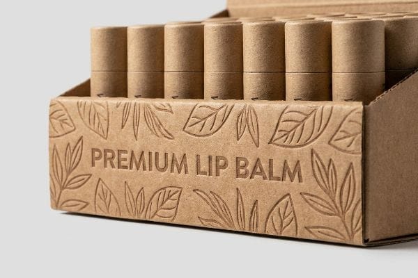 Debossed Premium Lip Balm Kraft paperboard display with debossed 'Premium Lip Balm' text and leaf patterns, showcasing sustainable lip balm tubes.