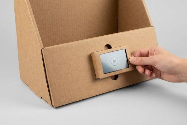 Entfernung des digitalen Bildschirms Display aus brauner Wellpappe mit einer Hand, die einen digitalen Bildschirm in eine gestanzte Reibungsverschlussvertiefung einsetzt, um die Hardware leicht entnehmen zu können.