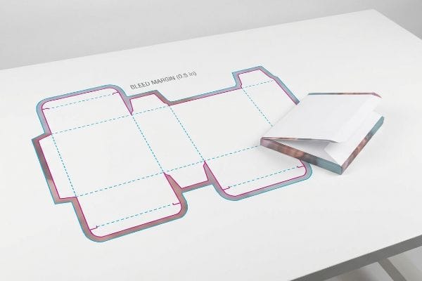 Dieline Bleed Margin Example A flat packaging dieline showing magenta and cyan lines with a 'Bleed Margin (0.5 In)' label, next to a partially folded box highlighting the print bleed.