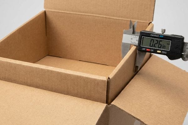 Box Wall Thickness Measurement Brown corrugated cardboard box wall measured by a digital caliper displaying 0.26 inches thickness.