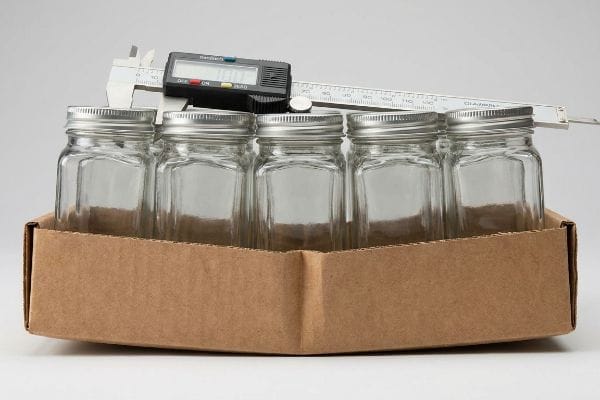 Spice Jar Caliper Measurement Digital caliper measuring five empty 4 oz glass spice jars in a brown cardboard tray, showing precise dimensions for packaging.