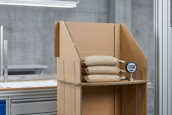 Display Structural Integrity Test Performing in-house structural testing on a corrugated cardboard display with sandbag weights and a digital gauge.