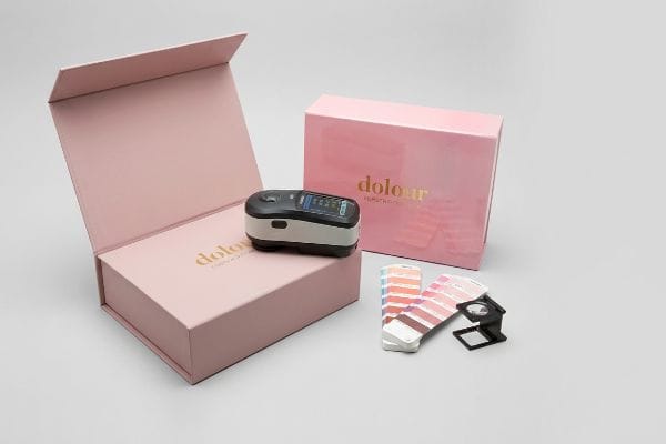 Dolour Color Measurement Kit A colorimeter on an open pink Dolour box, with color swatches and a closed box, for precise color measurement.