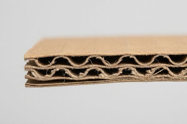Corrugated Board Cross-Section Close-up of brown double-wall corrugated paperboard, revealing two fluted layers and flat linerboards, showcasing the paper fiber matrix.