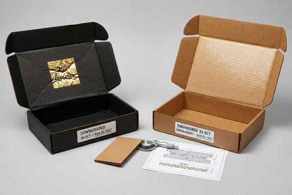 ECT-Box-Vergleichstest Schwarzer, abgewerteter 26 ECT-Versandkarton, der den Test nicht bestanden hat, und brauner, optimierter 32 ECT-Karton aus Virgin Kraftpapier, der den Test bestanden hat, mit Mikrometer.