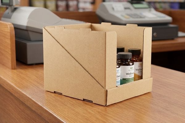ウェルネスカウンターディスプレイボックス 木製のレジカウンターの上に、「ウェルネストライアル」サプリメントのボトルを陳列した、段ボール製のEフルートカウンターディスプレイボックス。.