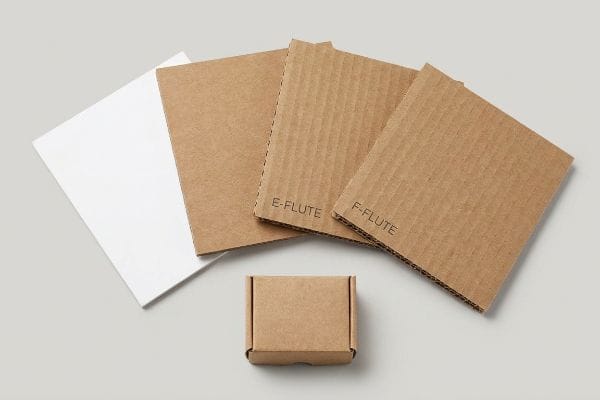 Corrugated Flute Types Box An overhead view shows E-Flute and F-Flute corrugated cardboard sheets, a white solid bleached sulfate sheet, and a small brown tuck box.