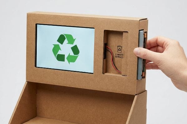 E-Waste Extraction Display Corrugated display with LCD recycling symbol, hand inserting battery into E-Waste Extract slot, showcasing friction-lock e-waste extraction.