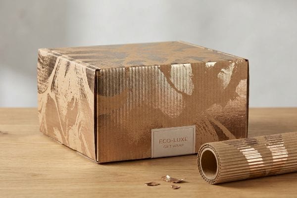 Eco-Luxe Gift Wrap Eco-Luxe Gift Wrap box and roll with metallic cold foil leaf pattern on fluted corrugated cardboard, showing metallic flakes.