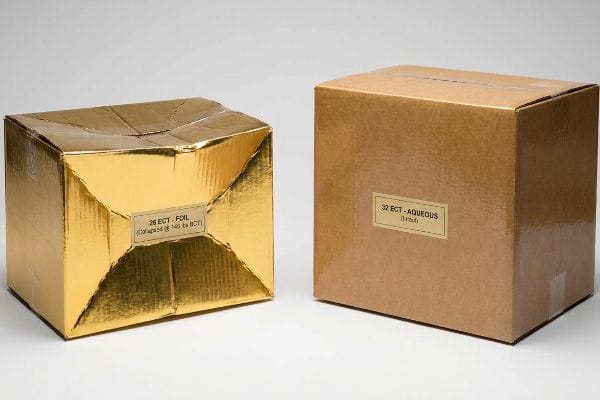 Packaging Strength Comparison A gold foil 26 ECT box, collapsed at 145 lbs BCT, stands beside an intact 32 ECT aqueous brown cardboard box.