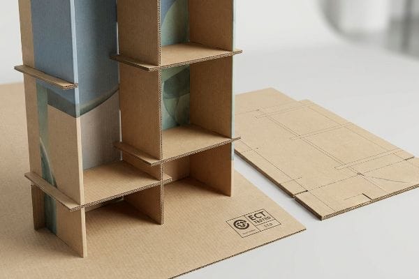 Corrugated Display ECT Tested An innovative corrugated display unit, partially assembled, showcases its modular design alongside flat fluted paperboard pieces marked "ECT Tested 11.0" and abstract blue-green graphics.