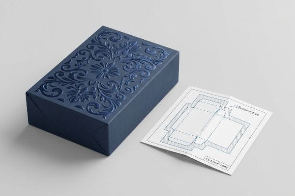 Embossed Box Dieline Zones Dark blue box with 3D embossed floral pattern next to a dieline showing Embossing Exclusion Zones for structural folds.