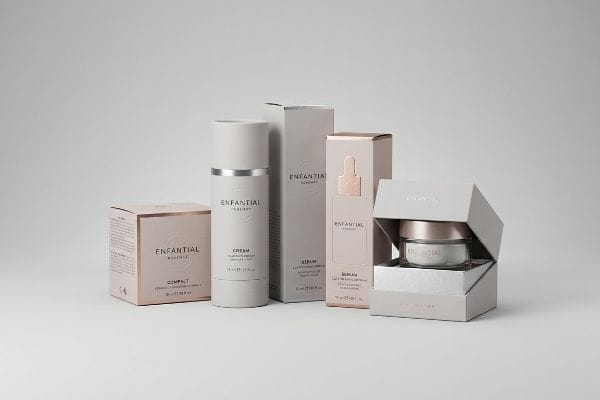 Various Enfantial cosmetic products, including Compact, Cream, and Serum, displayed in minimalist light grey and pink packaging with silver accents.