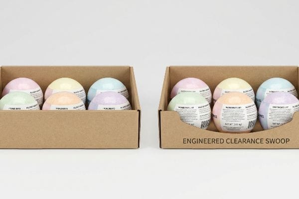 Engineered Swoop Display Tray Brown cardboard display trays, one with Engineered Clearance Swoop, hold pastel bath bombs showing 'Ingredients List' and 'Net Wt. 250G'.