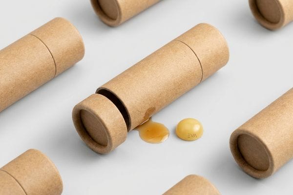 EVA Balm Migration Kraft paperboard tube with spilled essential oil and a yellow EVA balm pellet, illustrating solvent migration.