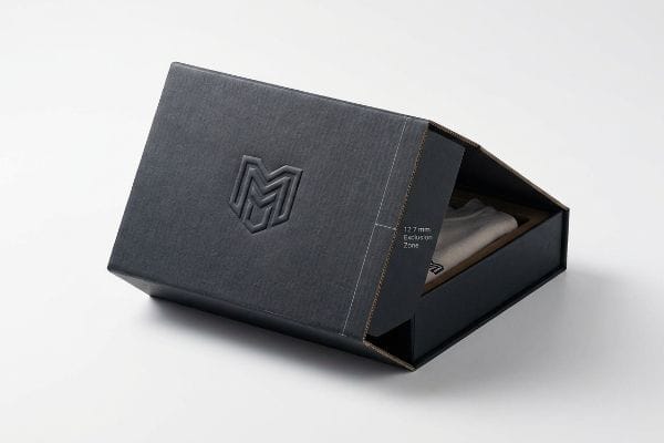 Embossing Exclusion Zone Box Dark grey textured gift box with an embossed M logo on the lid, partially open to show a 12.7 mm Exclusion Zone on the inner flap.