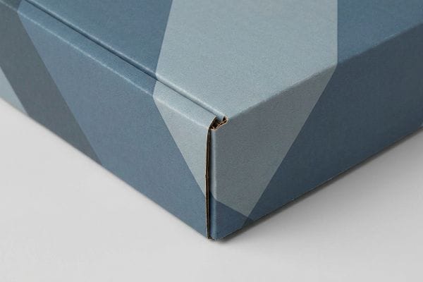 ボックスコーナーの印刷不良 青い幾何学模様が描かれた段ボール箱の角をクローズアップした写真。印刷時のずれによる欠陥で、紙板の端がむき出しになっているのがわかる。.