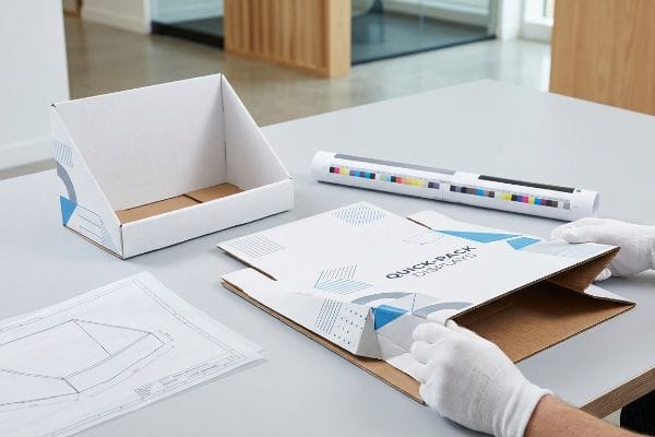 Assembling a Quick-Pack Displays E-flute flat-pack counter display box, with a finished unit and blueprint.