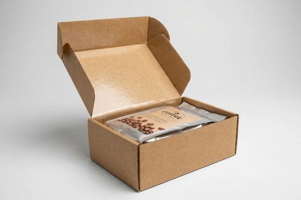 Coffee Box Packaging Brown corrugated cardboard box open, revealing a silver foil pouch of roasted Coffee beans inside, ideal for food-safe packaging.