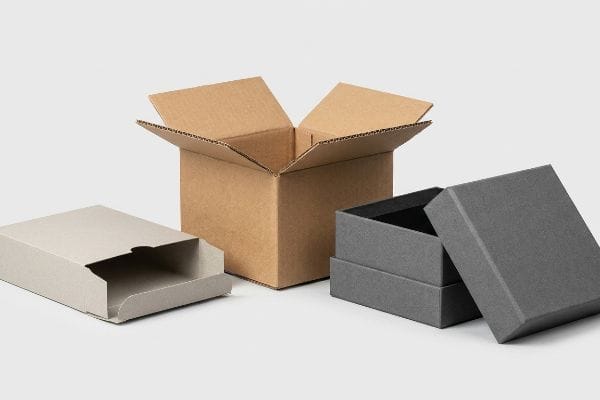 Light grey paperboard folding carton, open brown corrugated box, and dark grey rigid chipboard box with lid, showcasing diverse packaging types.