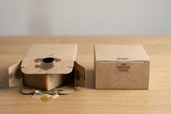 Kraft paperboard box with dissolved PVA adhesive failure, showing fragrance oil stains and sticky residue next to an intact EVA Adhesive Secure box.