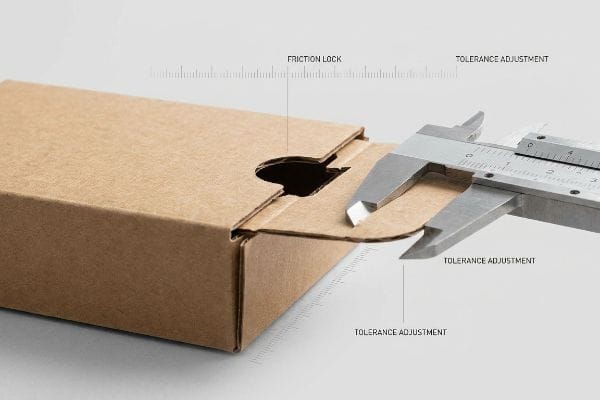 Tuck Box Caliper Measurement Brown corrugated cardboard tuck box flap being measured by a silver caliper, highlighting Friction Lock and Tolerance Adjustment for precise fit.