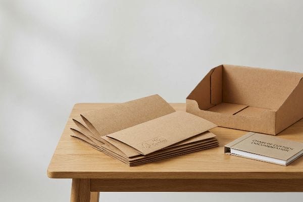Sustainable Packaging Documentation FSC Certified kraft paper mailers stacked next to an empty corrugated display tray and a Chain Of Custody Documentation book.