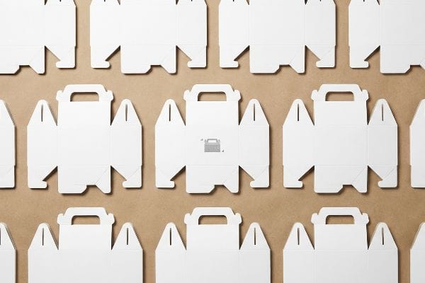White Gable Box Dielines Unfolded white cardboard dielines for custom gable boxes, featuring fold-over handles and auto-locking bottom flaps, arranged on a brown surface.