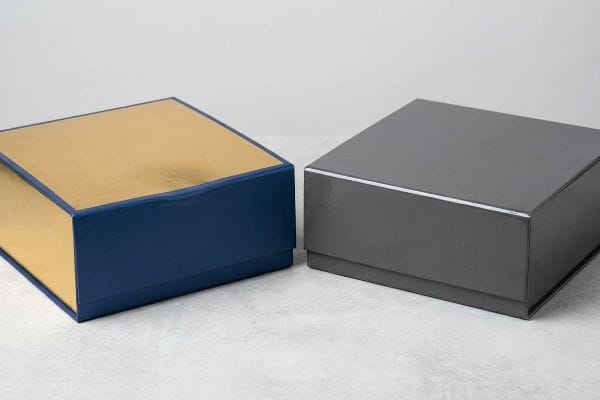Shiny dark blue and gold rigid gift box beside a glossy gray premium packaging.