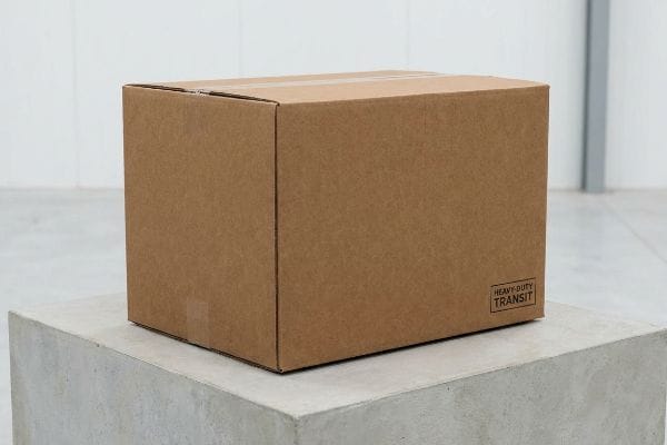 A brown cardboard shipping box, labeled 'Heavy-Duty Transit', rests on a concrete block, ideal for secure logistics.