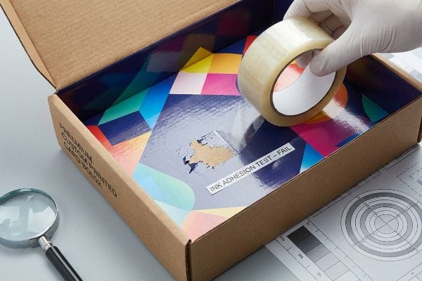 Brown cardboard box with a glossy, geometric printed liner showing an 'Ink Adhesion Test - Fail' label and peeled ink, highlighting poor adhesion for 'Premium Custom Printed Card Box'.
