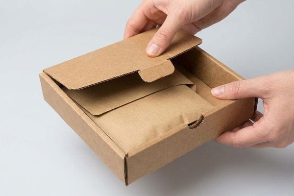 Hands opening a brown corrugated box with an intelligent paper lock, revealing an item wrapped in kraft paper.