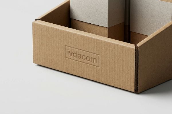 Primer plano de una bandeja expositora de cartón corrugado marrón con el logotipo "ivdacom" grabado en relieve en su panel lateral, que muestra un embalaje táctil.