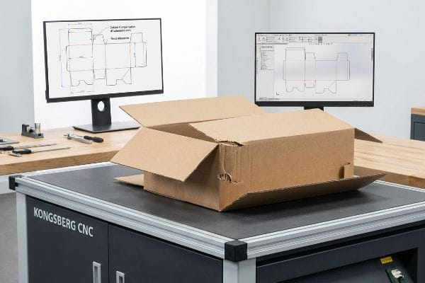 Caliper Compensation Dieline Design Kongsberg CNC table with open corrugated box, monitors display structural dielines for Caliper Compensation, Bend Allowance.