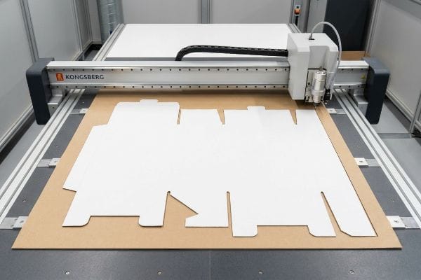 Kongsberg Dieline Cutting White virgin kraft board being precisely cut into a box dieline by a Kongsberg digital cutting table.